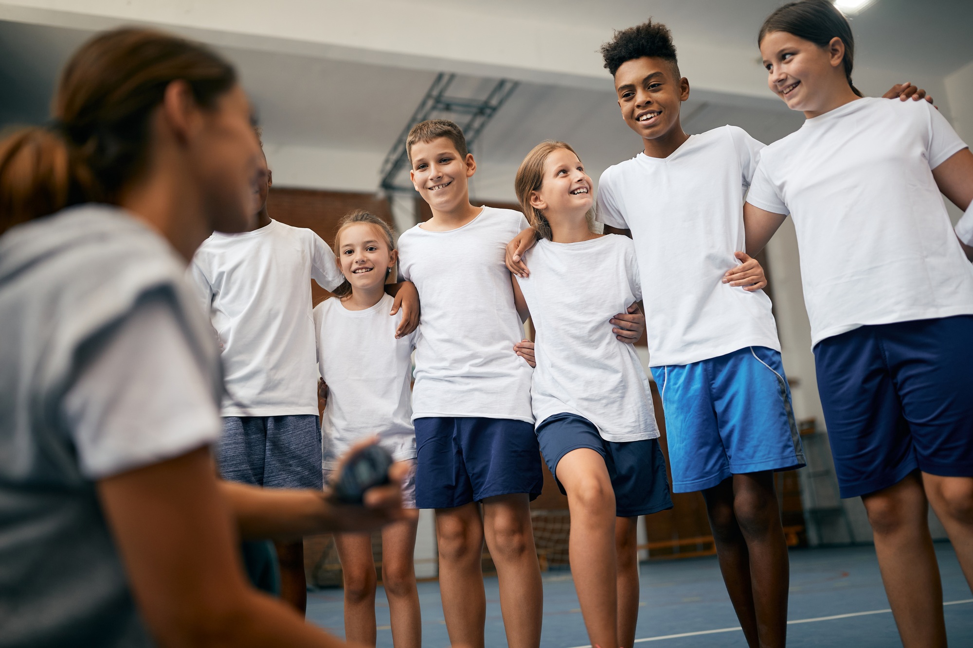 Happy school kids having physical education class with sports teacher at elementary school.