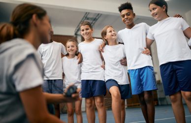 Happy school kids having physical education class with sports teacher at elementary school.