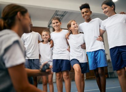 Happy school kids having physical education class with sports teacher at elementary school.